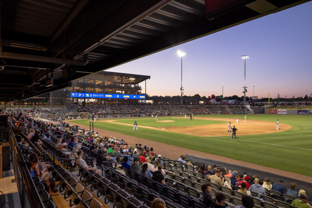 Erlanger Park - Chattanooga Lookouts - Packed baseball stadium at twilight with fans in dark bleachers, field lit by tall stadium lights, modern press box visible above home plate