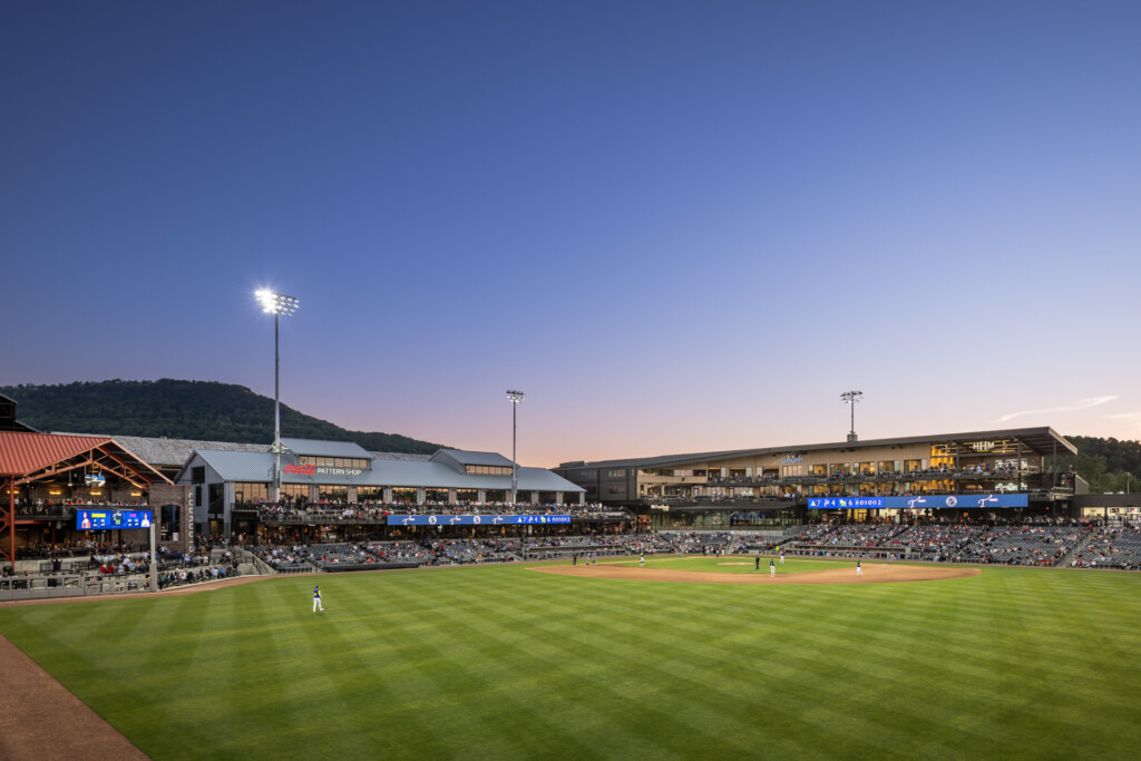 Erlanger Park - Chattanooga Lookouts - Minor league baseball stadium at twilight with field lights on, grandstands filled with spectators, and modern facility buildings under a purple-blue sky.