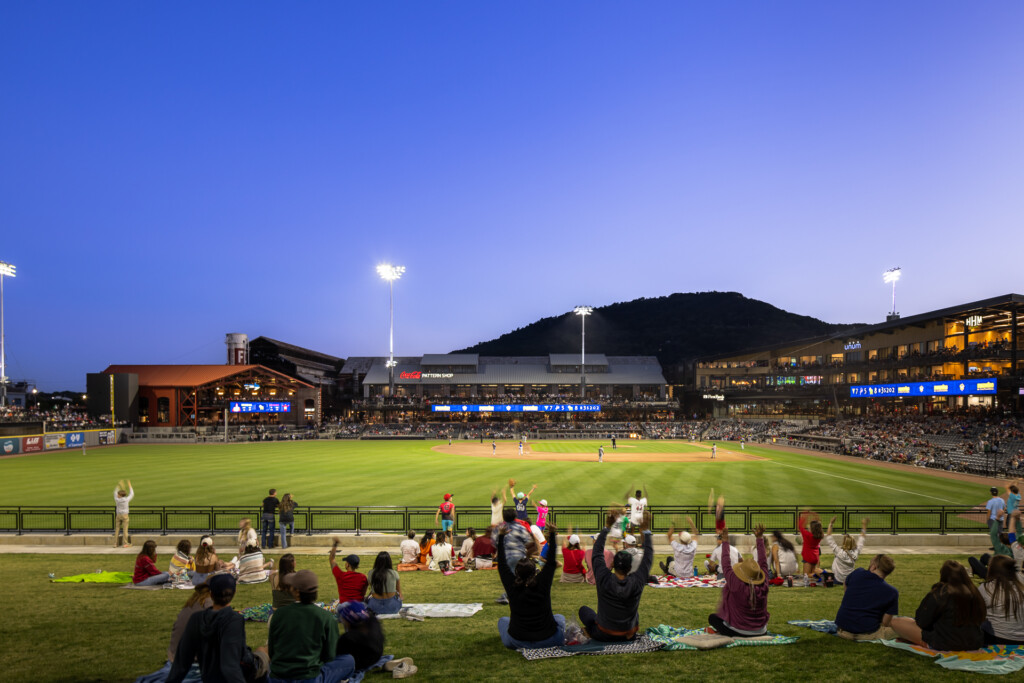 Erlanger Park - Chattanooga Lookouts - Fans sit on the grass in front of a lit baseball diamond at dusk, with grandstands and a mountain backdrop