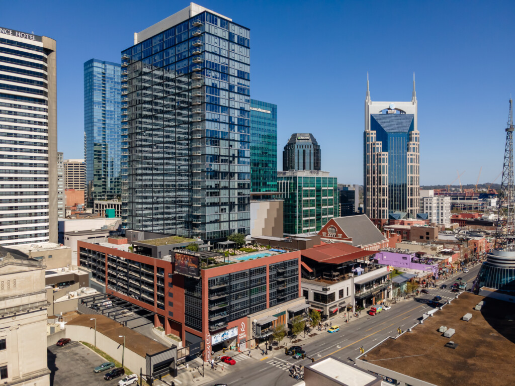Cityscape featuring mixed-use high-rise buildings, a distinctive spired landmark tower, and street-level retail with pedestrian activity under clear blue sky