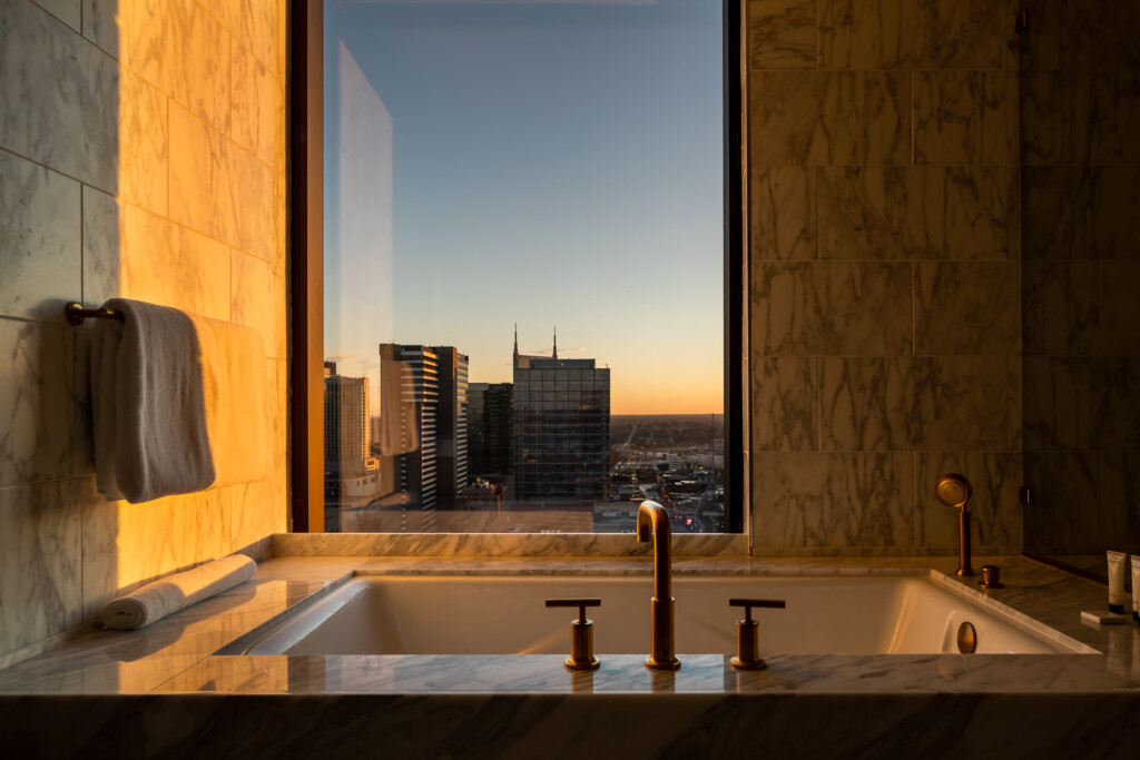 Marble bathroom with soaking tub and bronze fixtures overlooking downtown skyline at golden hour