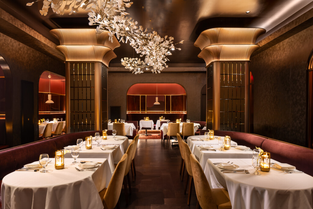 Philippe Chow - Nashville - Fine dining room with white-draped tables, sculptural brass columns, ornate crystal chandelier, and warm ambient lighting throughout the elegant space