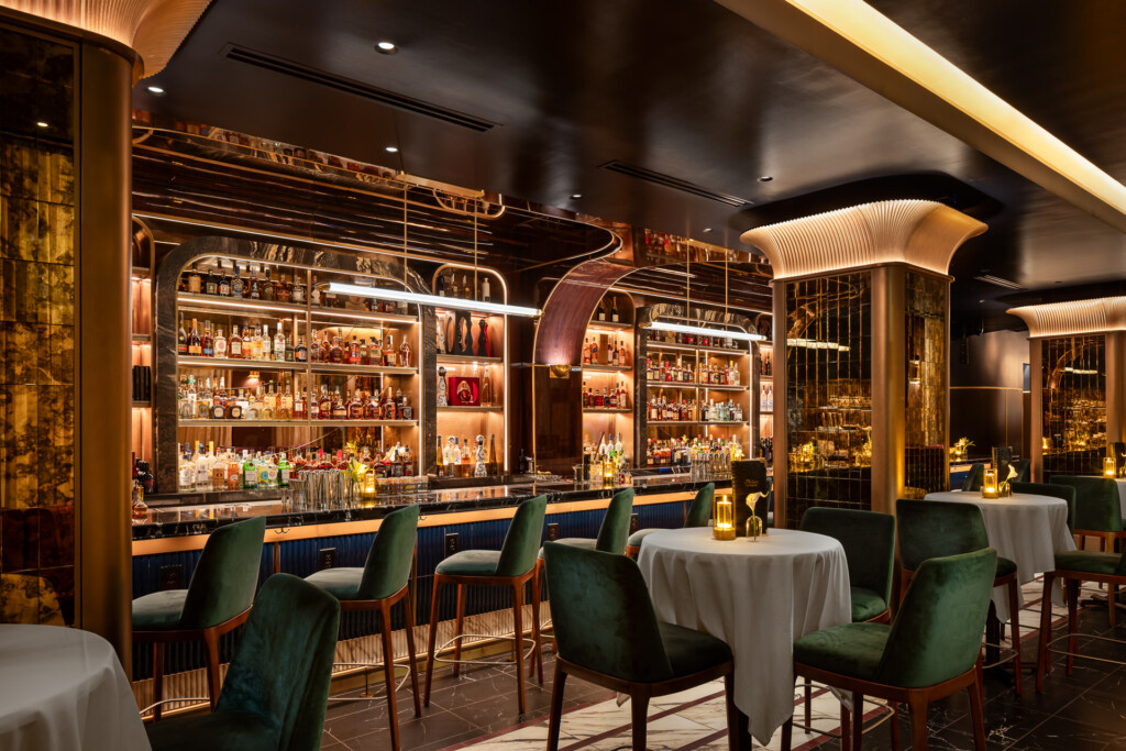Philippe Chow - Nashville - Upscale bar and restaurant interior with brass-framed shelving displaying spirits, green velvet dining chairs, white linens, and warm ambient lighting