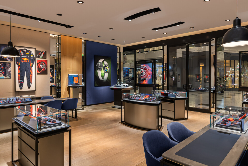 Spacious retail showroom with illuminated display cases, wood and glass cabinetry, navy accent walls, pendant lighting, and contemporary seating areas showcasing merchandise