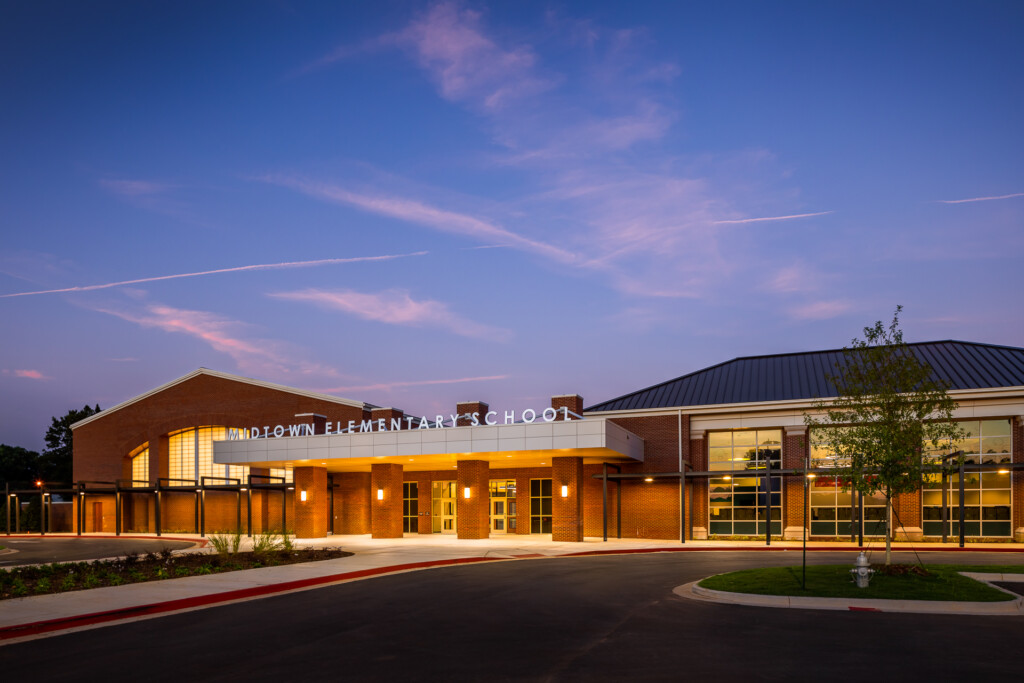 Modern brick elementary school building with illuminated interior and contemporary architecture photographed at dusk under blue sky