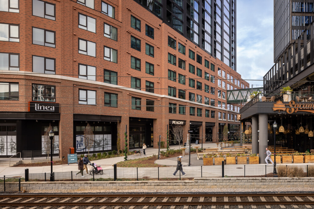 Linea at Southend - Red brick multifamily building with ground-floor storefronts, pedestrians, and outdoor seating area along a streetcar track