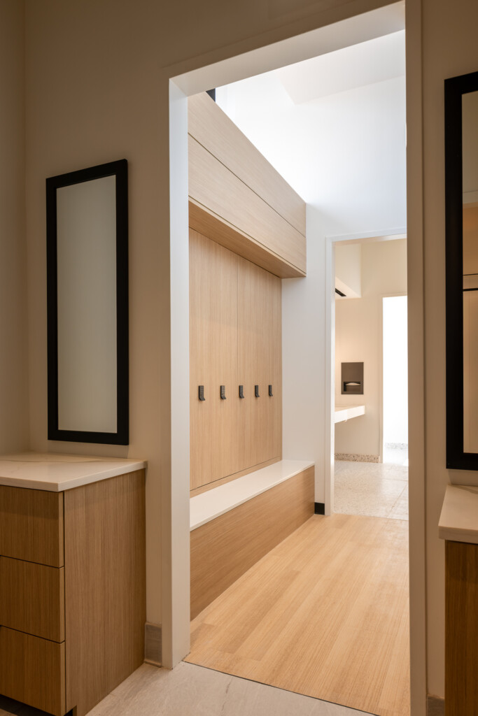 Olive at Peabody - Walk-in closet with vertical wood plank doors, white trim frame, and light wood flooring visible through the doorway. Wood dresser with black-framed mirror on left wall.