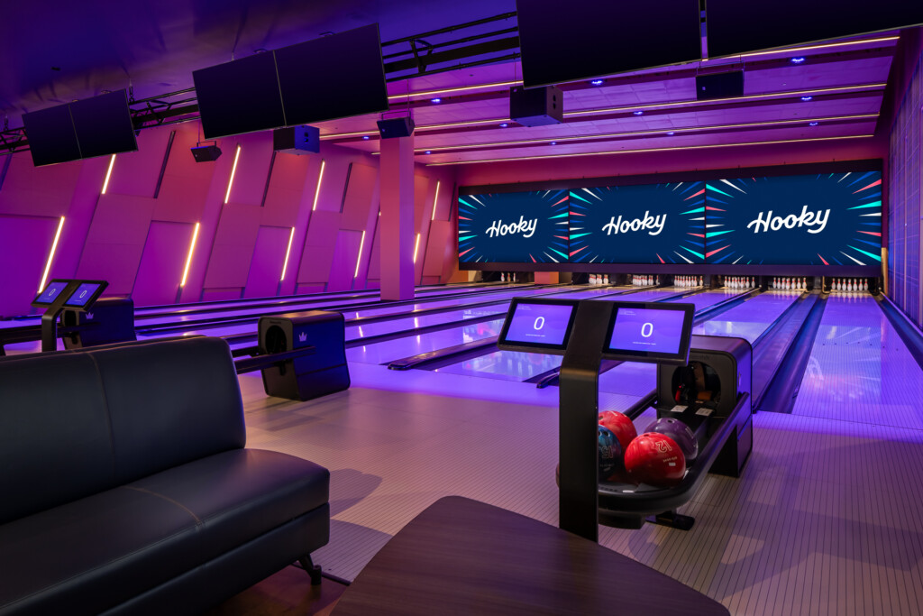 Hooky, Nashville Yards - Interior of a contemporary bowling facility featuring purple and magenta neon lighting, multiple lanes with scoring screens, red bowling balls, and a lounge area with dark seating.
