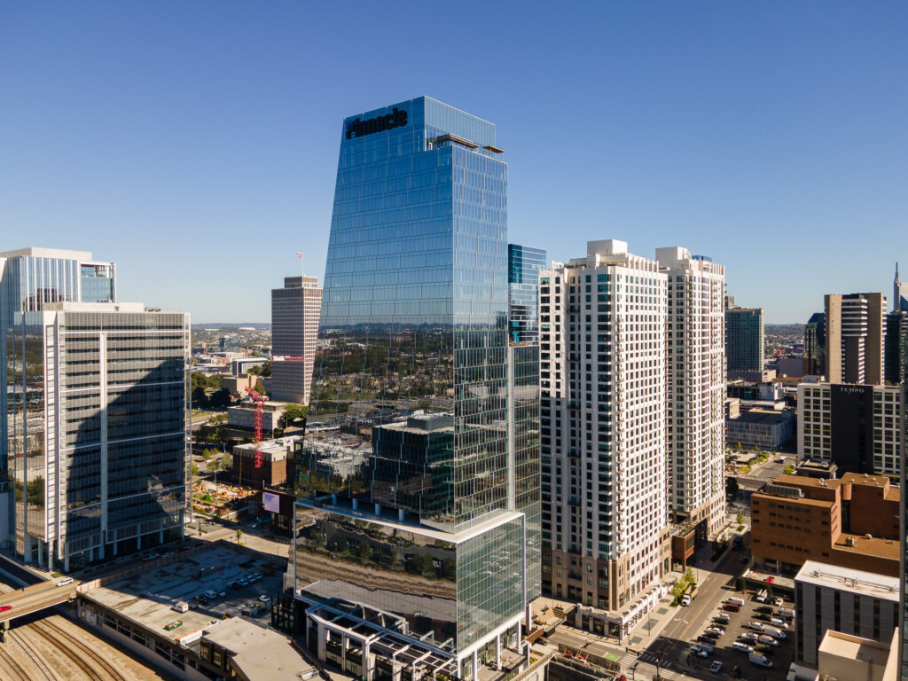 Urban skyline featuring contemporary glass and steel office towers with residential multifamily buildings, clear blue sky overhead