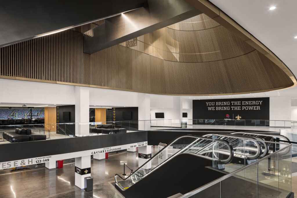 New Orleans Superdome - Open-concept commercial space with curved wood soffit, escalators, polished concrete floor, and signage reading 'You Bring the Energy We Bring the Power'