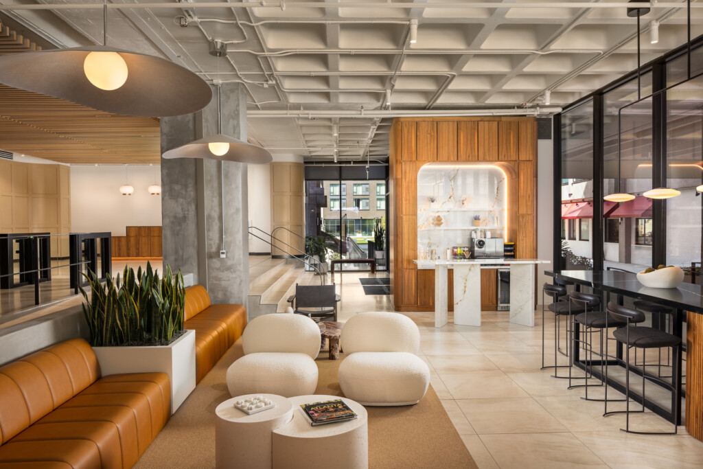 Open commercial space with coffered ceiling, orange leather seating, cream poufs, wood accent wall with illuminated display, and bar seating area