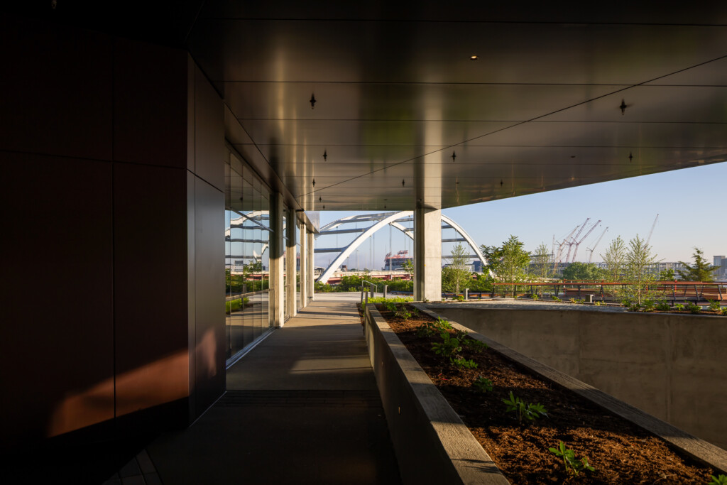 Covered terrace with concrete planter beds, steel columns, and floor-to-ceiling windows framing contemporary architecture beyond