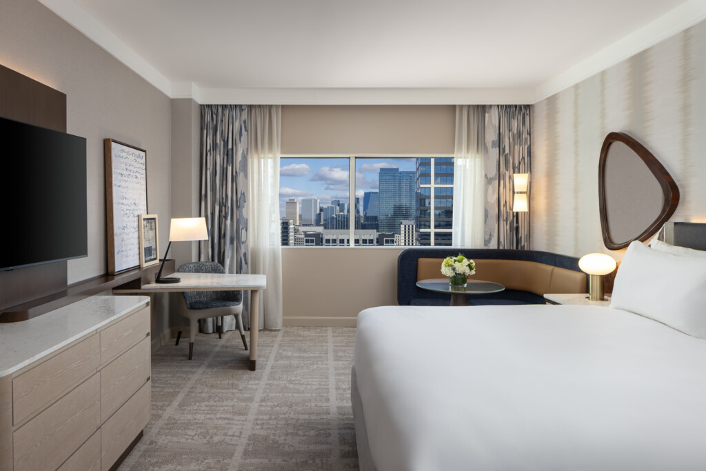 Loews Vanderbilt - Spacious hotel room with king bed, work desk, flat-screen TV, and floor-to-ceiling windows overlooking a city skyline