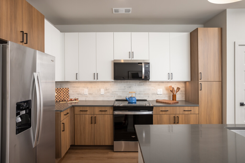 Contemporary kitchen with warm wood lower cabinets and white upper cabinets, stainless steel appliances, subway tile backsplash, and gray countertops.