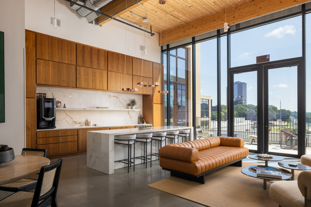Contemporary loft interior with wood-paneled kitchen, marble waterfall island, cognac leather sofa, and floor-to-ceiling windows overlooking city skyline