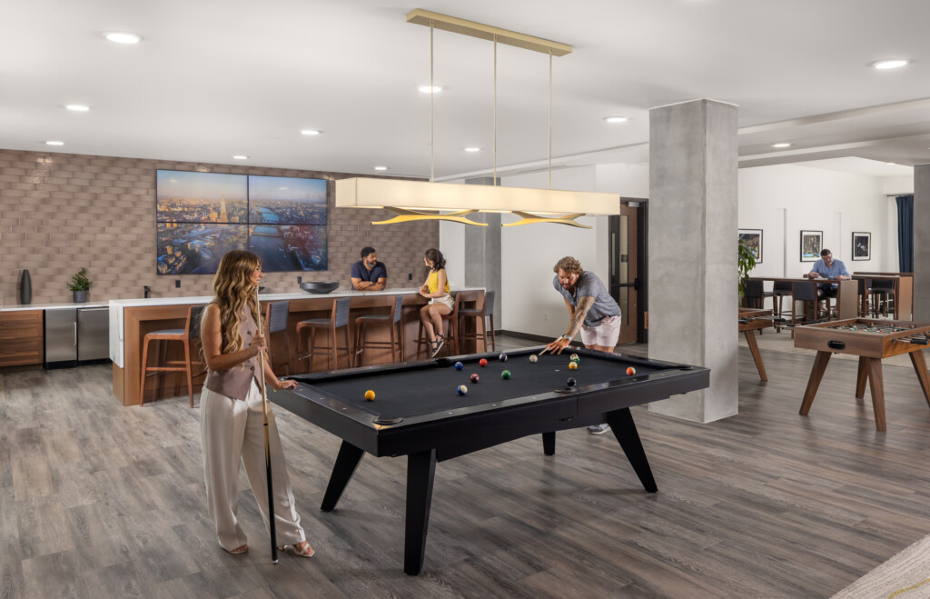 445 Park Commons - GEODIS - Open-concept recreation area with billiards table in foreground, bar seating along back wall, and lounge area visible through archway with foosball table