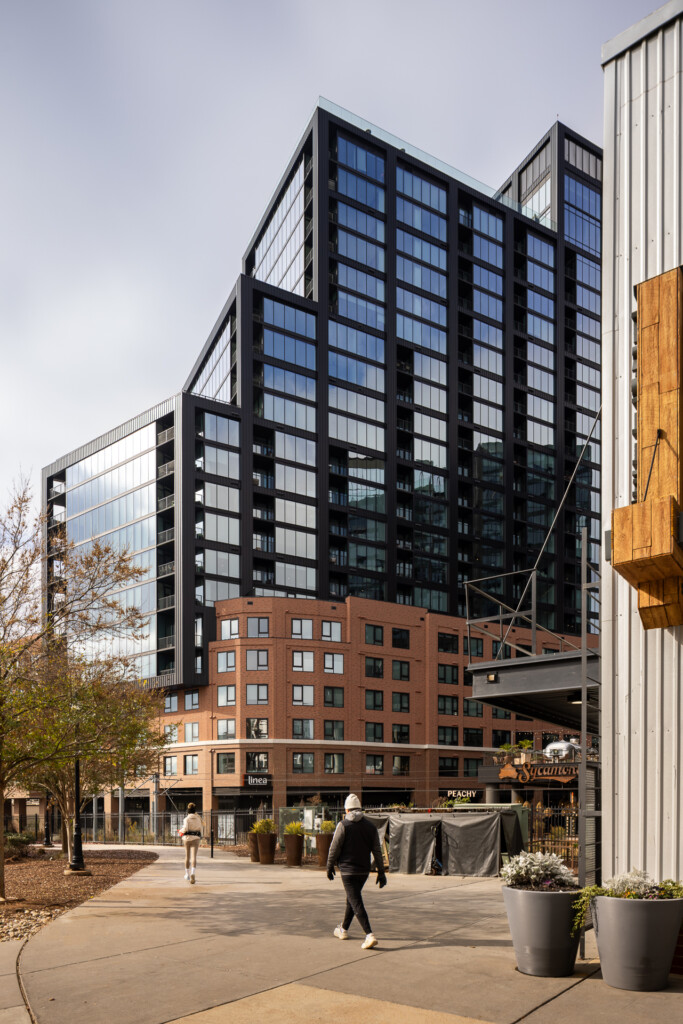 Linea at Southend - Charlotte - Contemporary multifamily building with black metal and glass upper stories over red brick base, street-level retail, and outdoor plaza with pedestrians and planters
