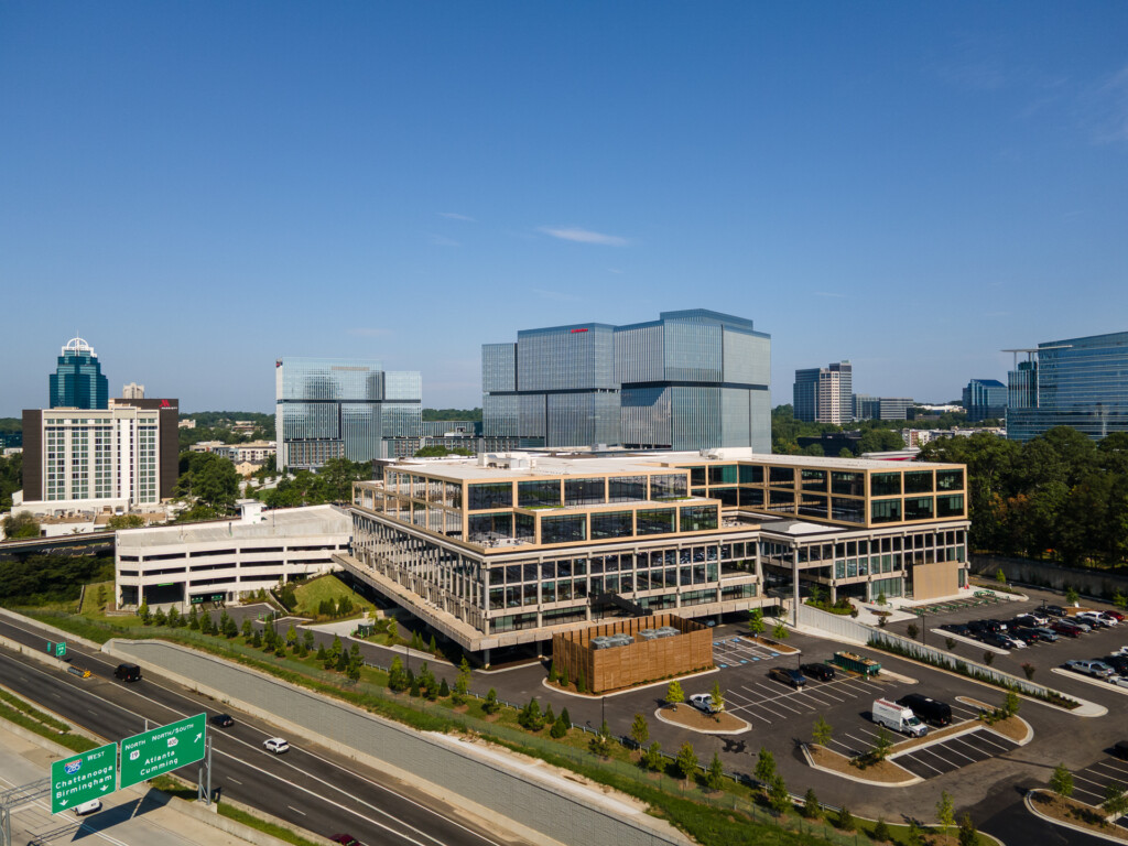 Contemporary multi-story commercial building with wood and glass facade, parking lot, and downtown skyline in background