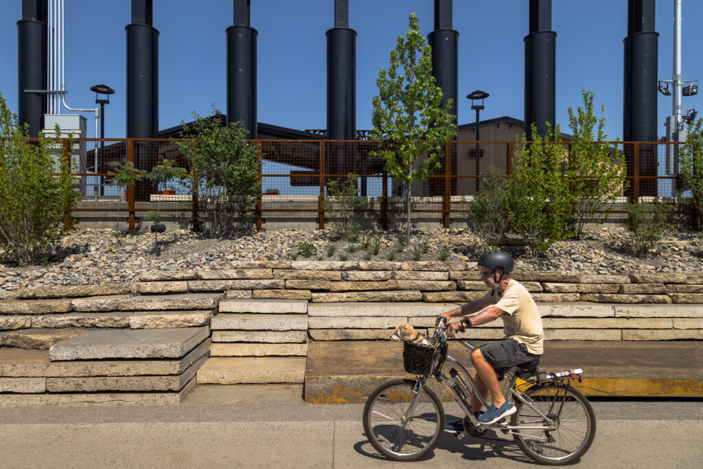 Erlanger Park - Chattanooga Lookouts - Person on bicycle rides past terraced stone seating steps in a riverside park, with tall black columns and landscaping visible in the background
