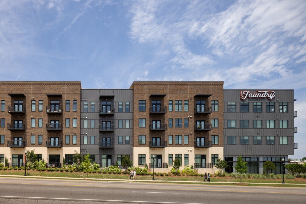 The Foundry Huntsville - Modern multifamily building with brick and metal cladding, ground-floor retail, and the Foundry sign, with manicured landscaping and clear blue sky