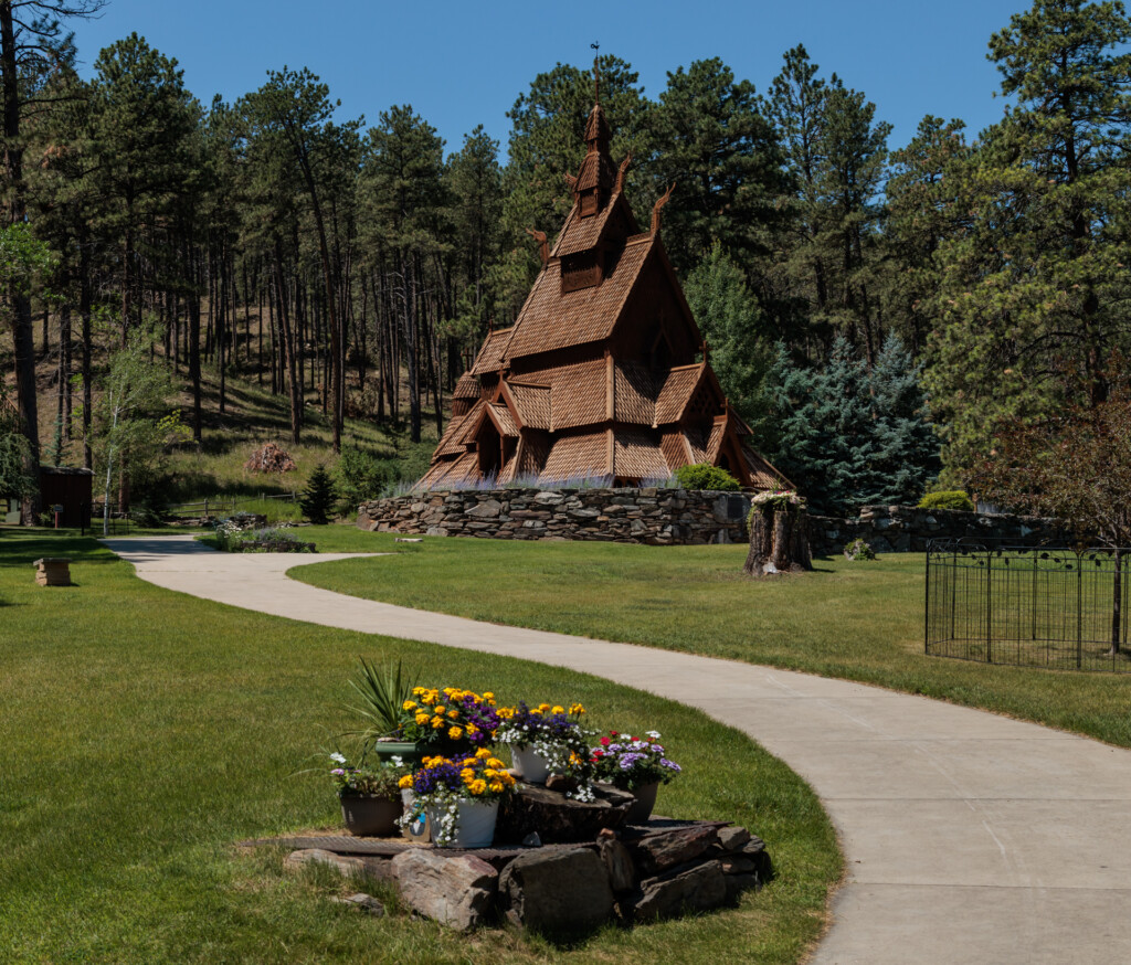 A distinctive building with soaring copper rooflines nestled in a pine forest, with manicured grounds, flowering planters, and winding concrete pathways
