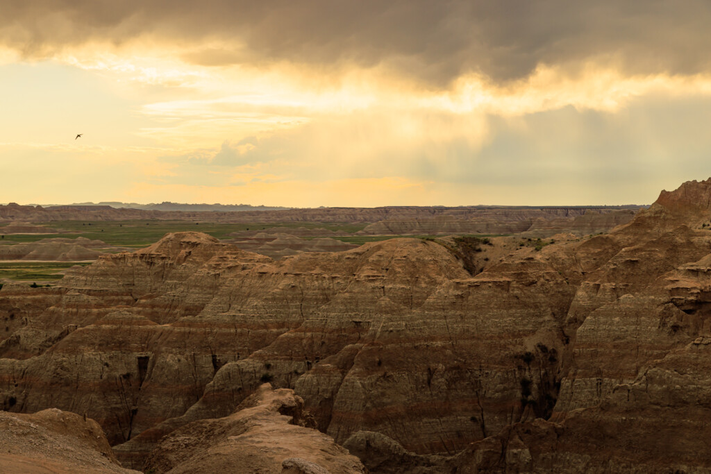 Layered badlands terrain with eroded buttes and valleys under warm sunlit clouds