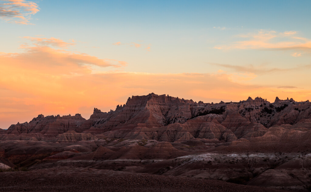 Rugged badlands terrain with layered rock formations silhouetted against a golden sunset sky