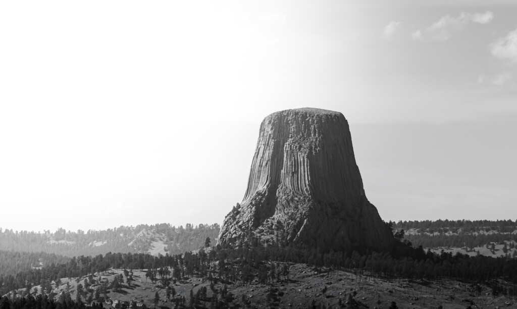 Distinctive columnar rock formation rises prominently from forested landscape under cloudy sky
