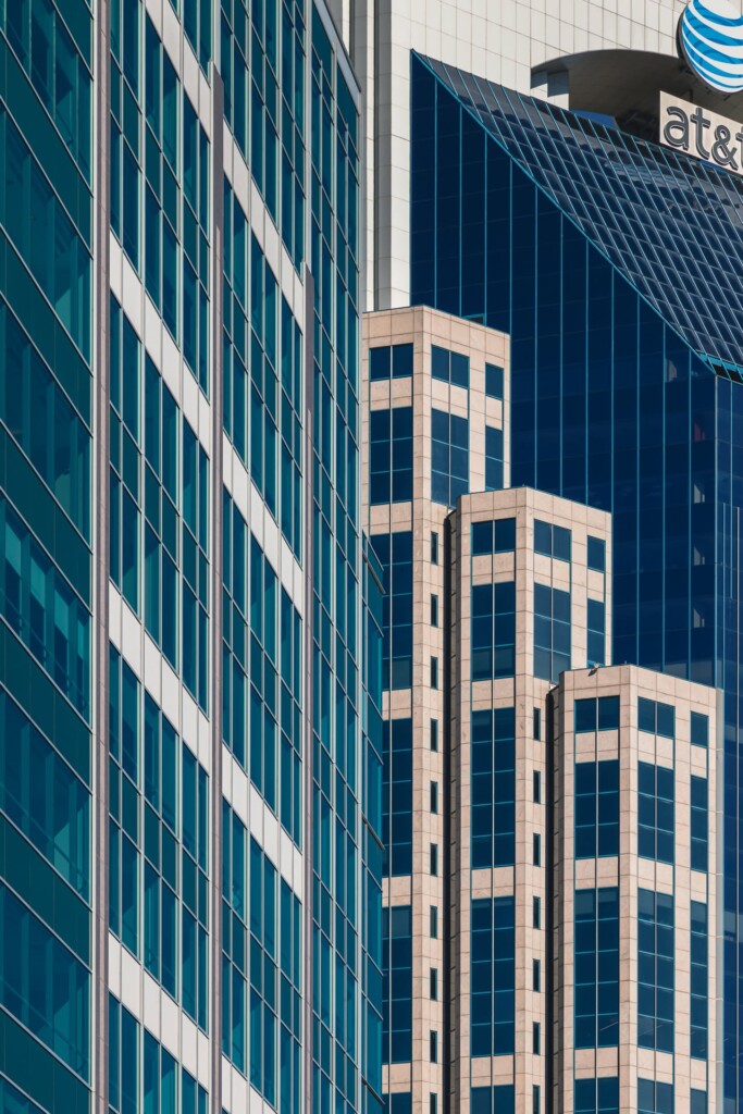 Geometric composition of modern office buildings with contrasting glass and stone facades, featuring vertical lines and a distinctive stepped tower design in the center.