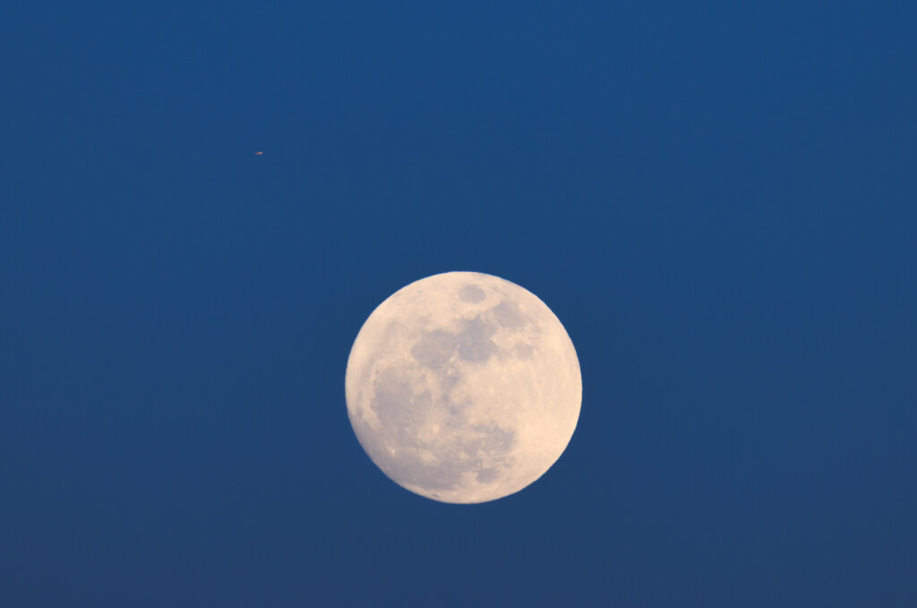 A luminous full moon with visible surface craters and maria against a deep blue twilight sky