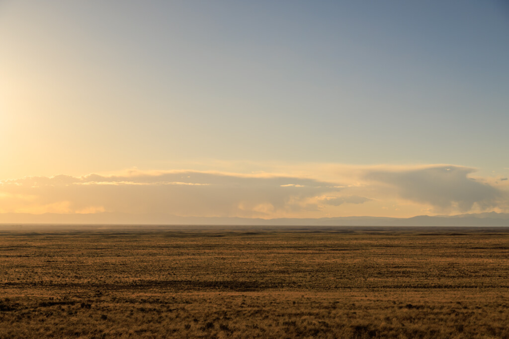 Wide open desert plain under a golden sky with towering clouds on the horizon at sunset