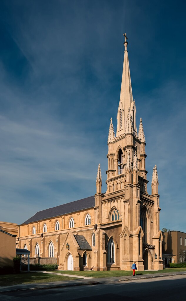 Cream-colored Gothic Revival church with tall pointed spire, pointed arch windows, and decorative stonework against blue sky