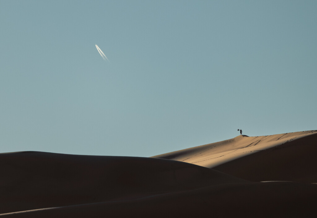 Silhouetted roofline of contemporary building with illuminated upper edge against blue sky, small human figure visible on ridge