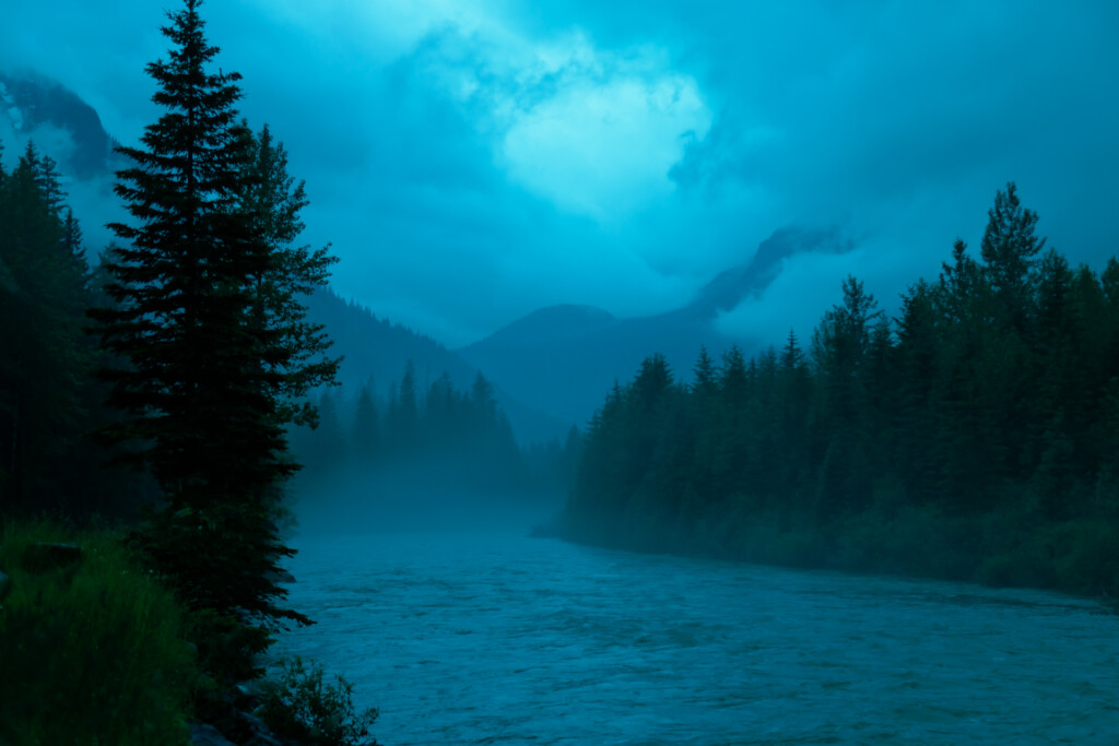 Misty mountain lake surrounded by dense evergreen forest under twilight sky with clouds