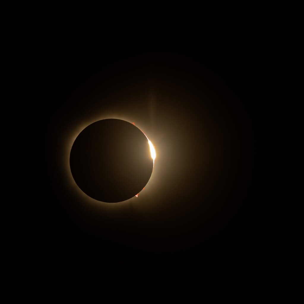 Moon silhouetted against sun's corona during total eclipse, bright light flaring on right edge